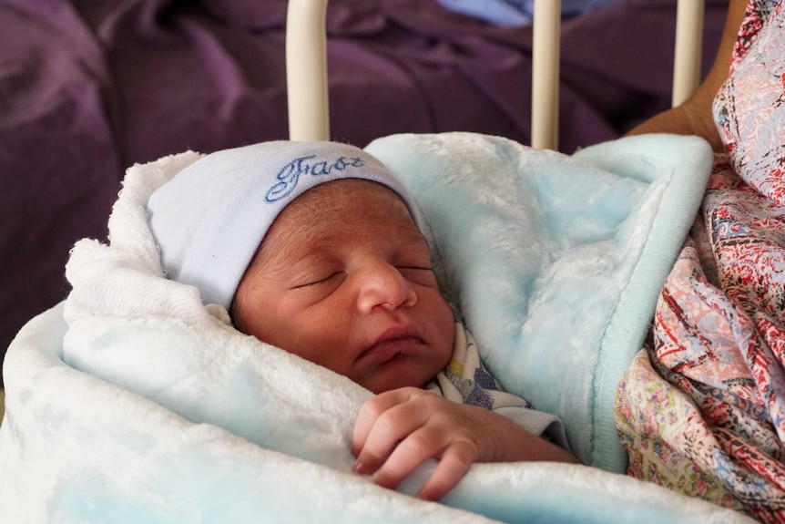 A newborn baby wrapped in a blue blanket snuggled in his mother's arms