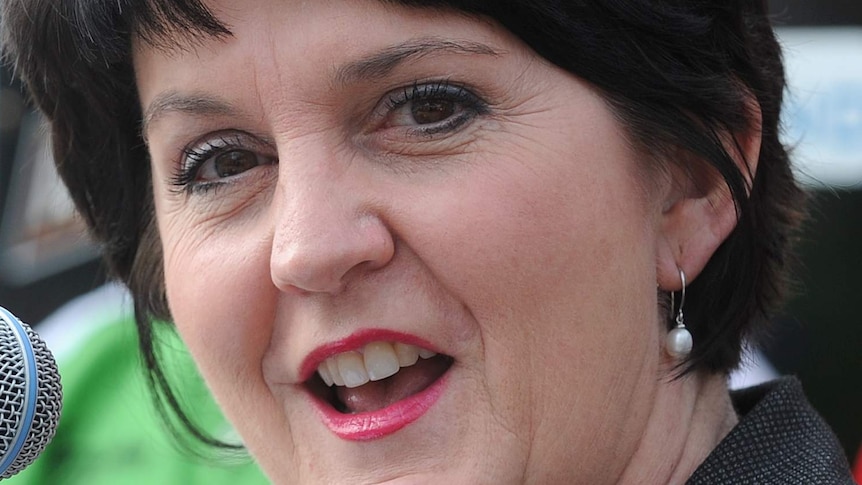 Jann Stuckey wears red lipstick, in a tight head shot next to a microphone.