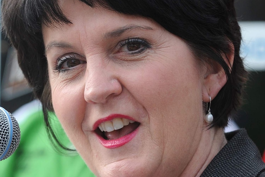 Jann Stuckey wears red lipstick, in a tight head shot next to a microphone.