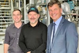 Three men smiling in front of a large piece of industrial machinery.