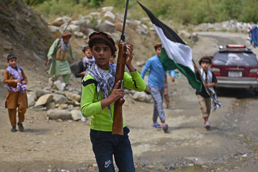 Children of local Afghan residents carrying hunting rifles and a flag