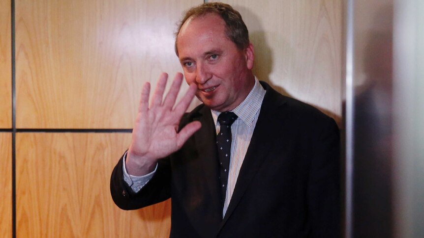 Deputy Prime Minister Barnaby Joyce waves at reporters with his right hand.