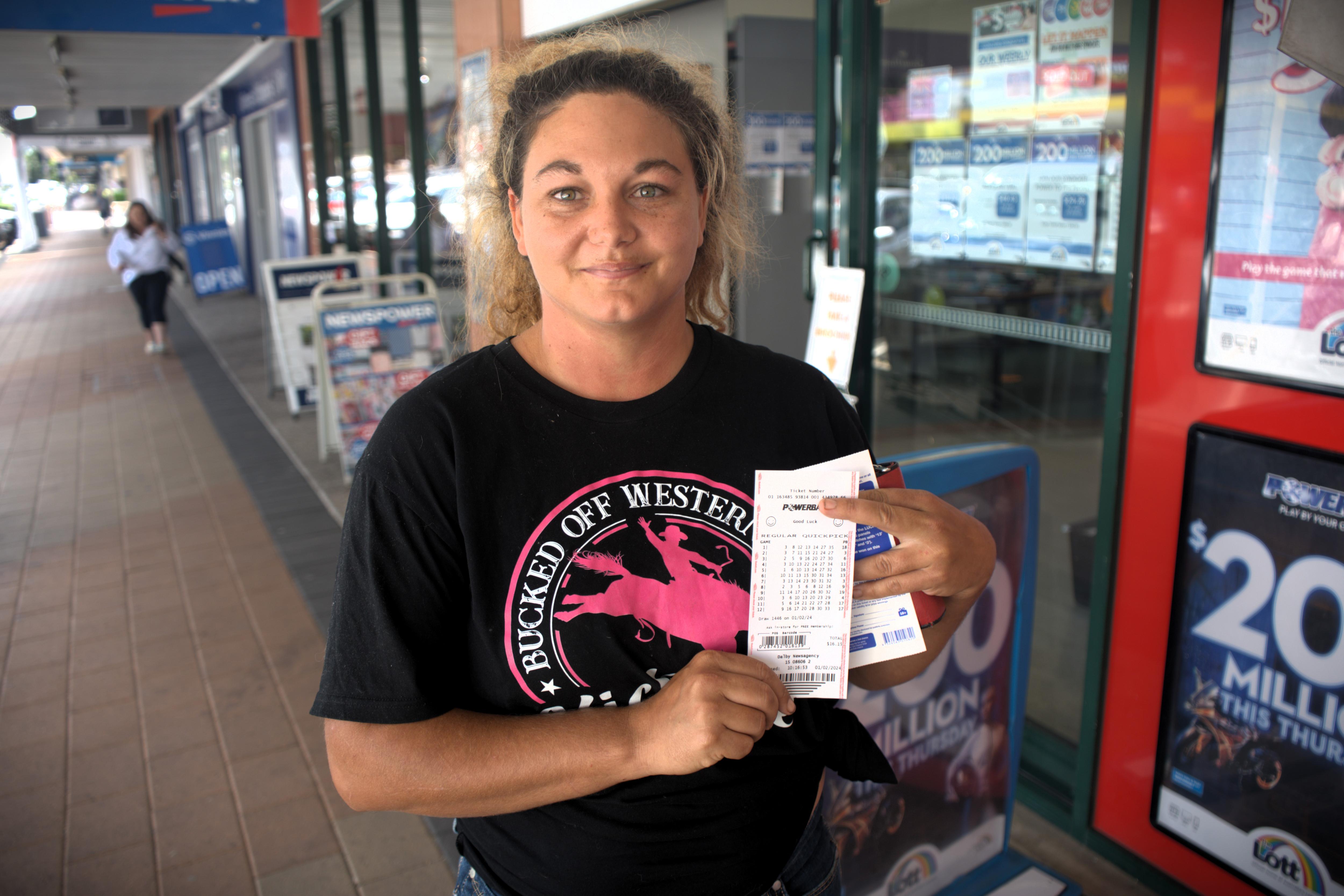 A woman stands outside a newsagency holding a lotto ticket