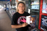 A woman stands outside a newsagency holding a lotto ticket