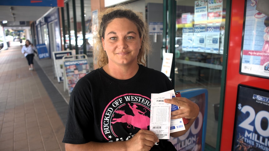 A woman stands outside a newsagency holding a lotto ticket