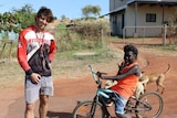 A guy stands next to a young indigenous kid on a bike