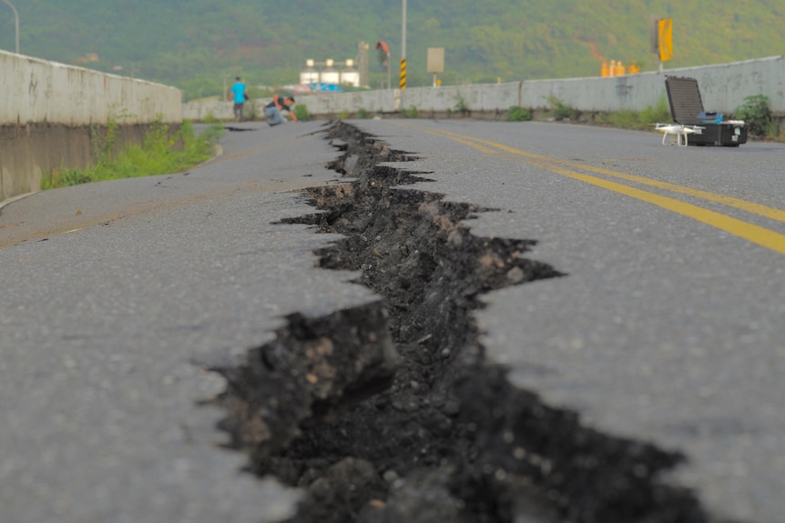 A large crack runs throuhg the middle of a highway road. 