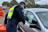 A Victoria Police officer checks a driver's licence and permit at a highway checkpoint