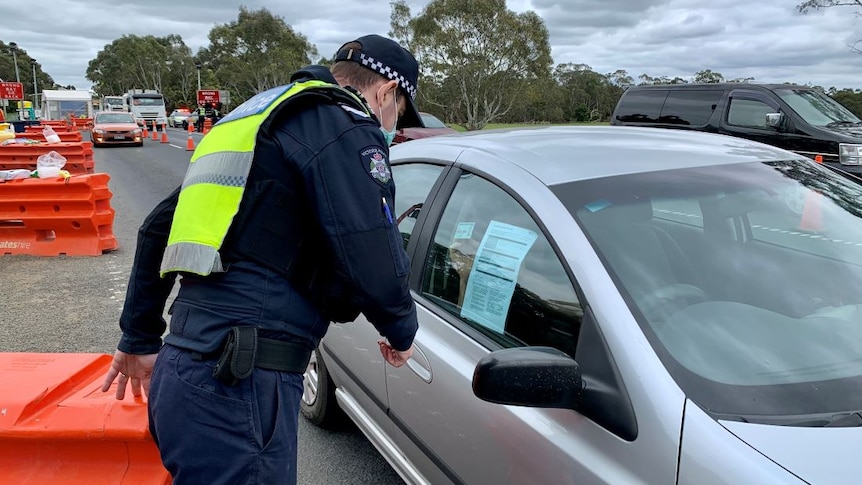 A Victoria Police officer checks a driver's licence and permit at a highway checkpoint