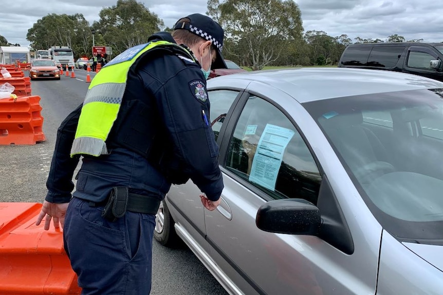 A Victoria Police officer checks a driver's licence and permit at a highway checkpoint