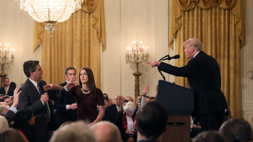 A White House staff member reaches for the microphone held by CNN's Jim Acosta as he questions Donald Trump.