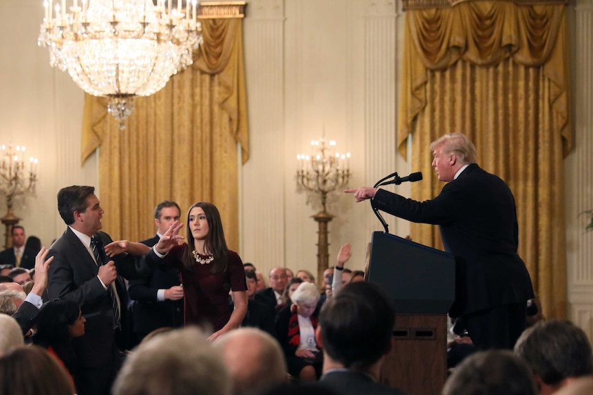 A White House staff member reaches for the microphone held by CNN's Jim Acosta as he questions Donald Trump.