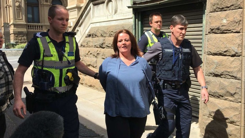 A woman is escorted from court by police in yellow vests.
