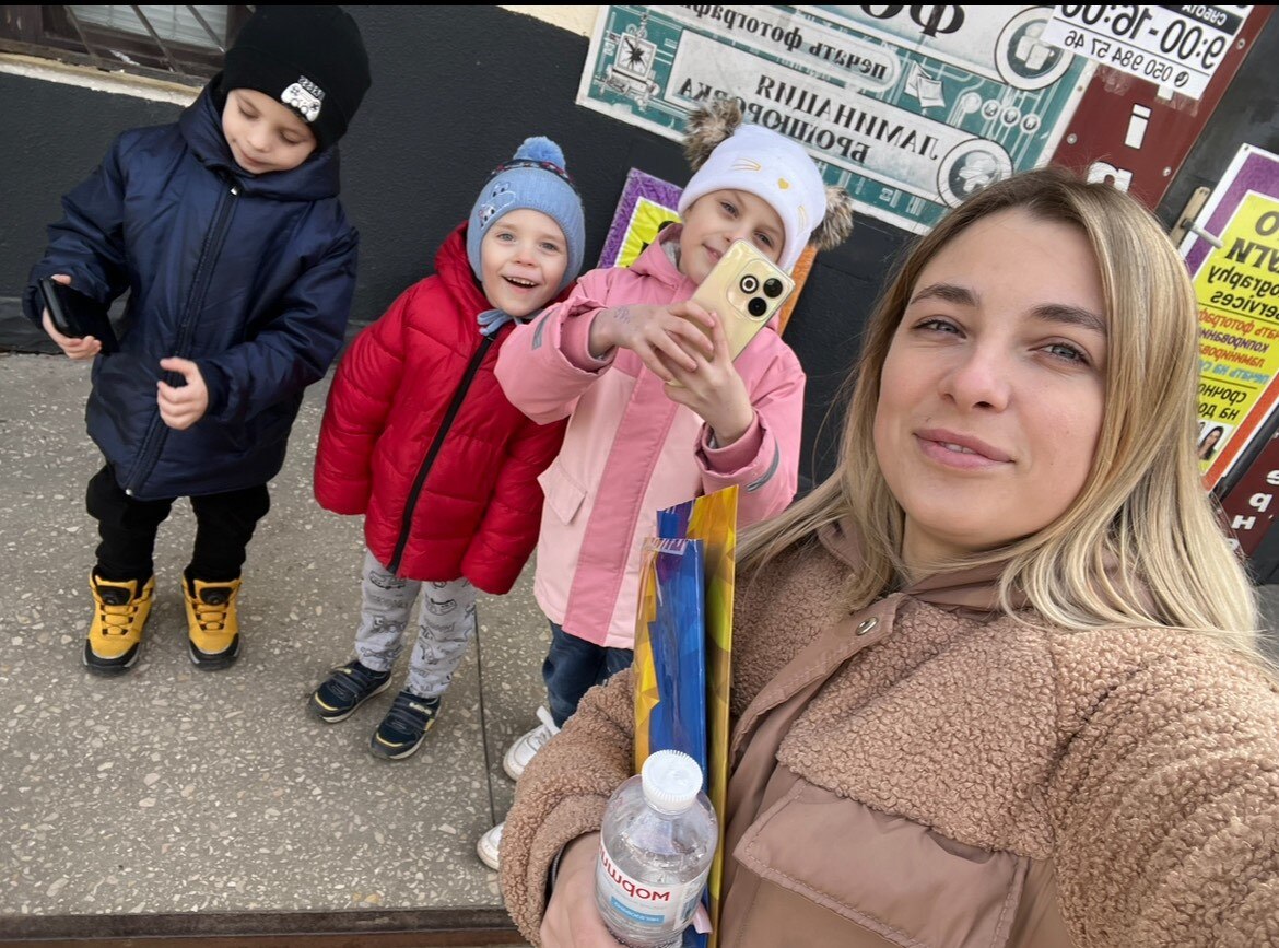 A young woman and her two yound sons and daughter pose for a selfie in the street.