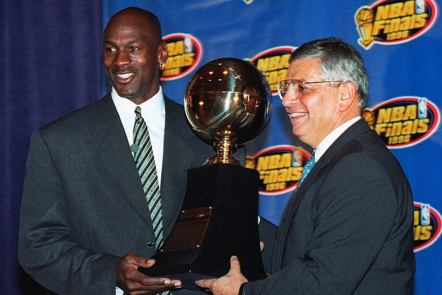 Michael Jordan in a suit holding the NBA Finals MVP trophy with david stern in a suit