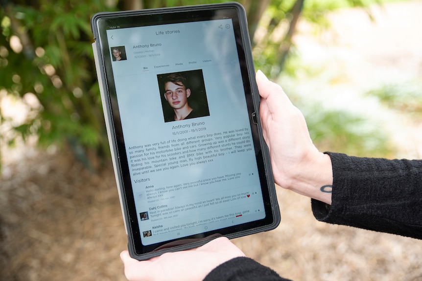 Two hands hold out a tablet with information about the late Anthony Bruno