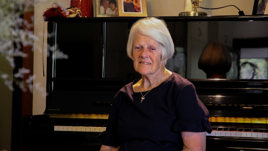 An elderly woman with medium-length grey hair sitting in front of a black piano.