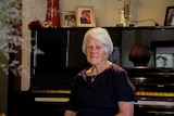 An elderly woman with medium-length grey hair sitting in front of a black piano.