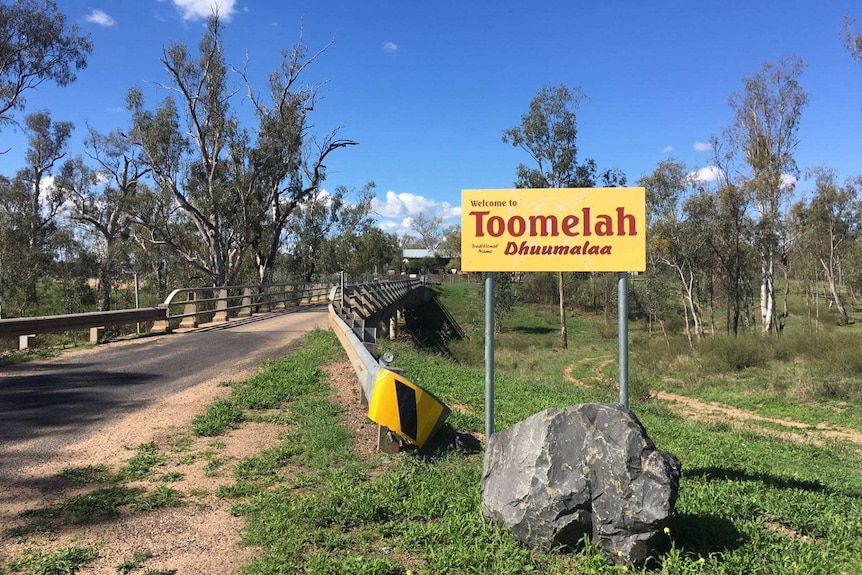 A yellow sign says 'Welcome to Toomelah' next to a road bridge.
