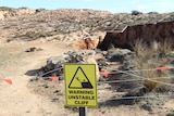 A yellow sign reading 'warning unstable cliff' with a barricade and coastal hole behind