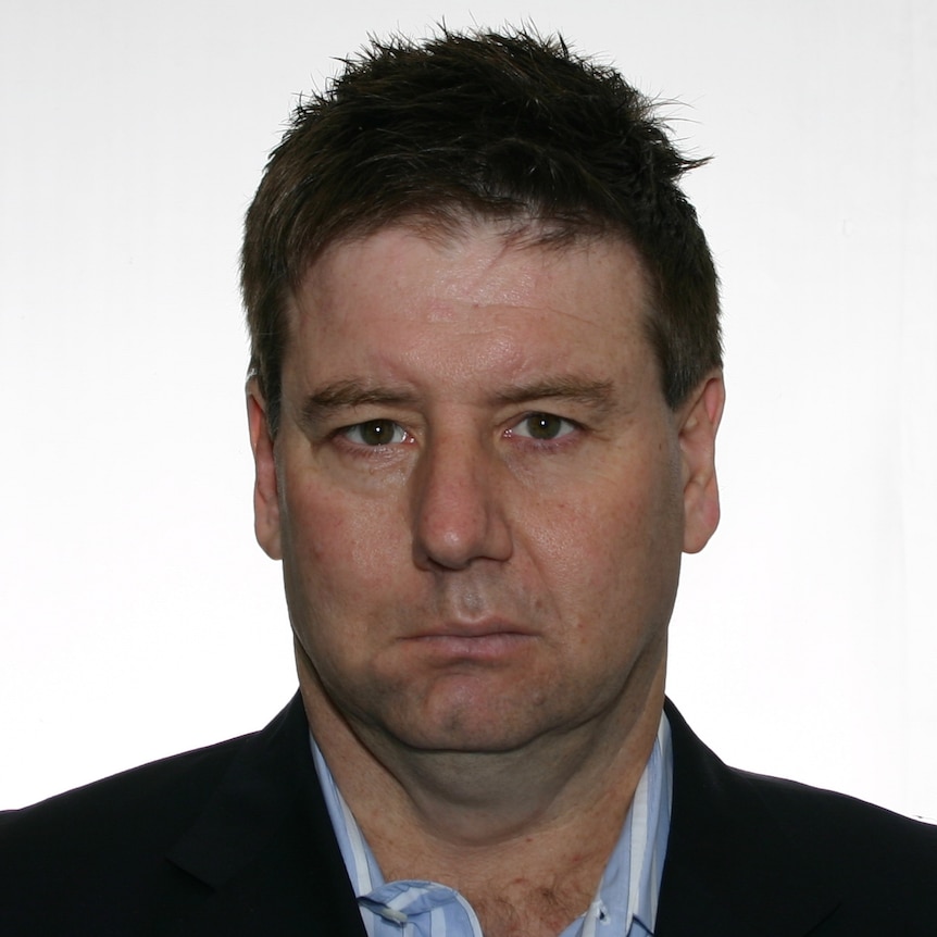 A middle-aged man looks into the camera with a serious expression.