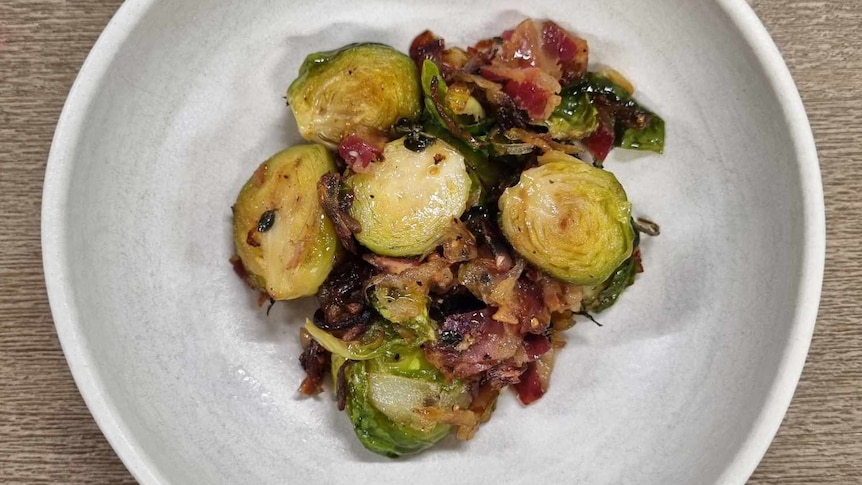 Waji's cooked brussel sprouts containing speck, olive oil, herbs and more, in a bowl.