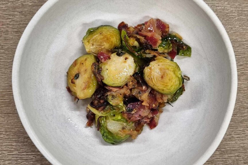Waji's cooked brussel sprouts containing speck, olive oil, herbs and more, in a bowl.