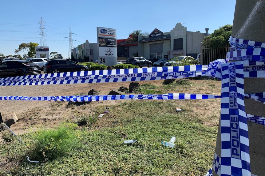 Police crime scene tape in the foreground with an industrial estate behind.