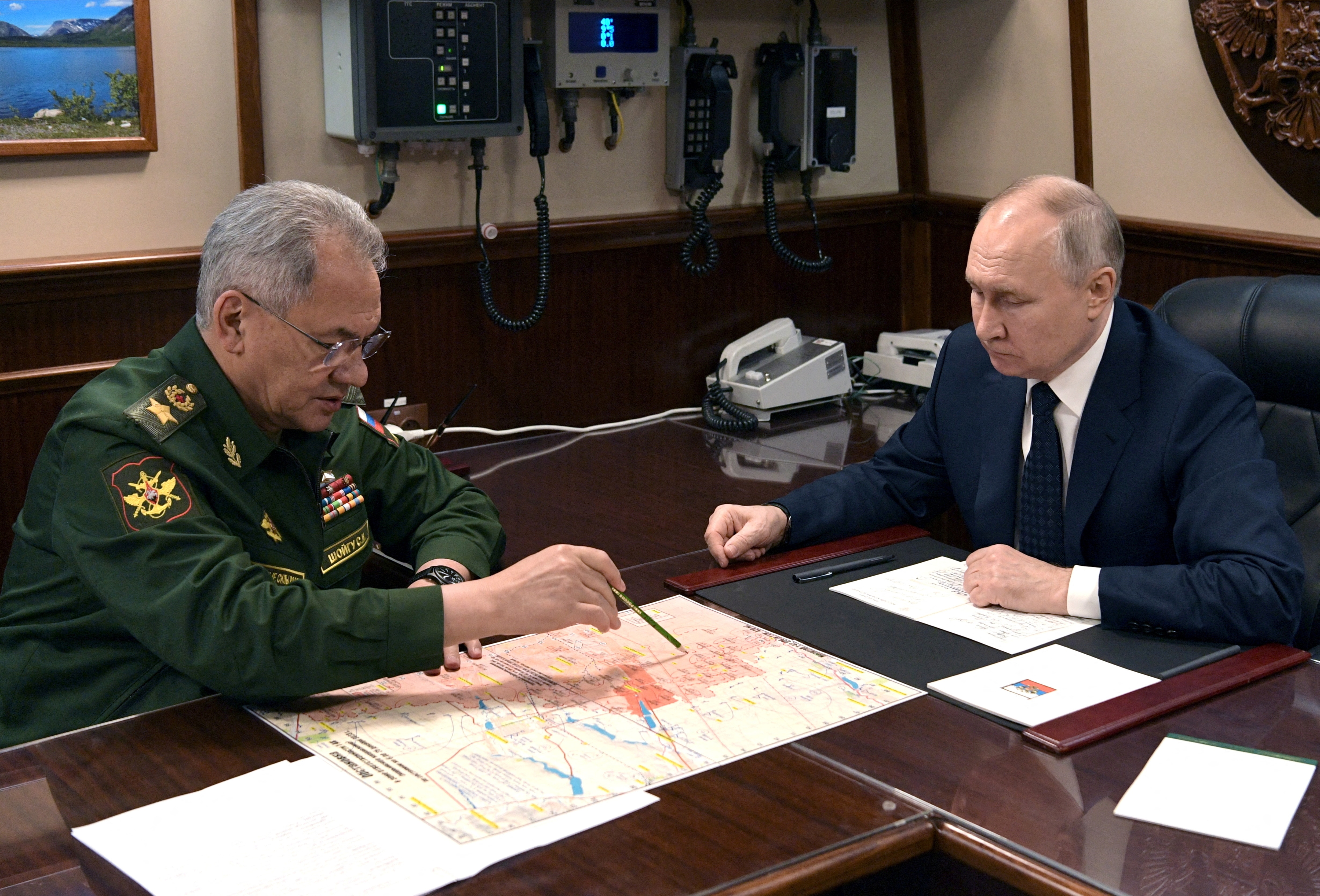  Vladimir Putin and Sergei Shoigu sitting across from eachother at a table. 