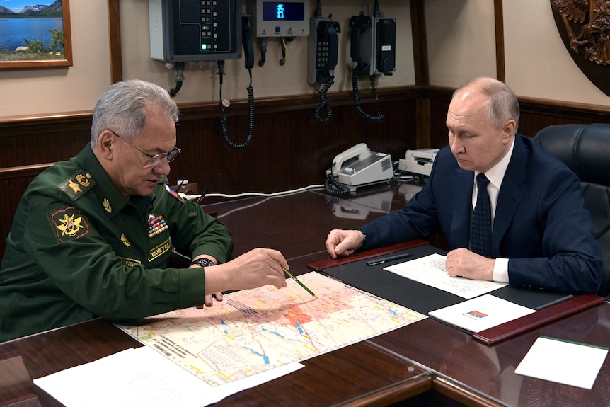  Vladimir Putin and Sergei Shoigu sitting across from eachother at a table. 