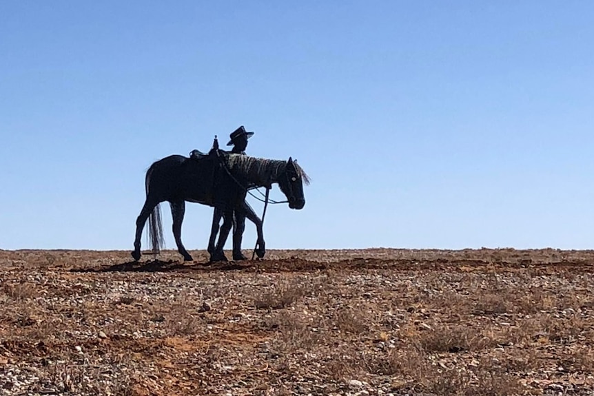 a metallic man and horse in the barren landscape