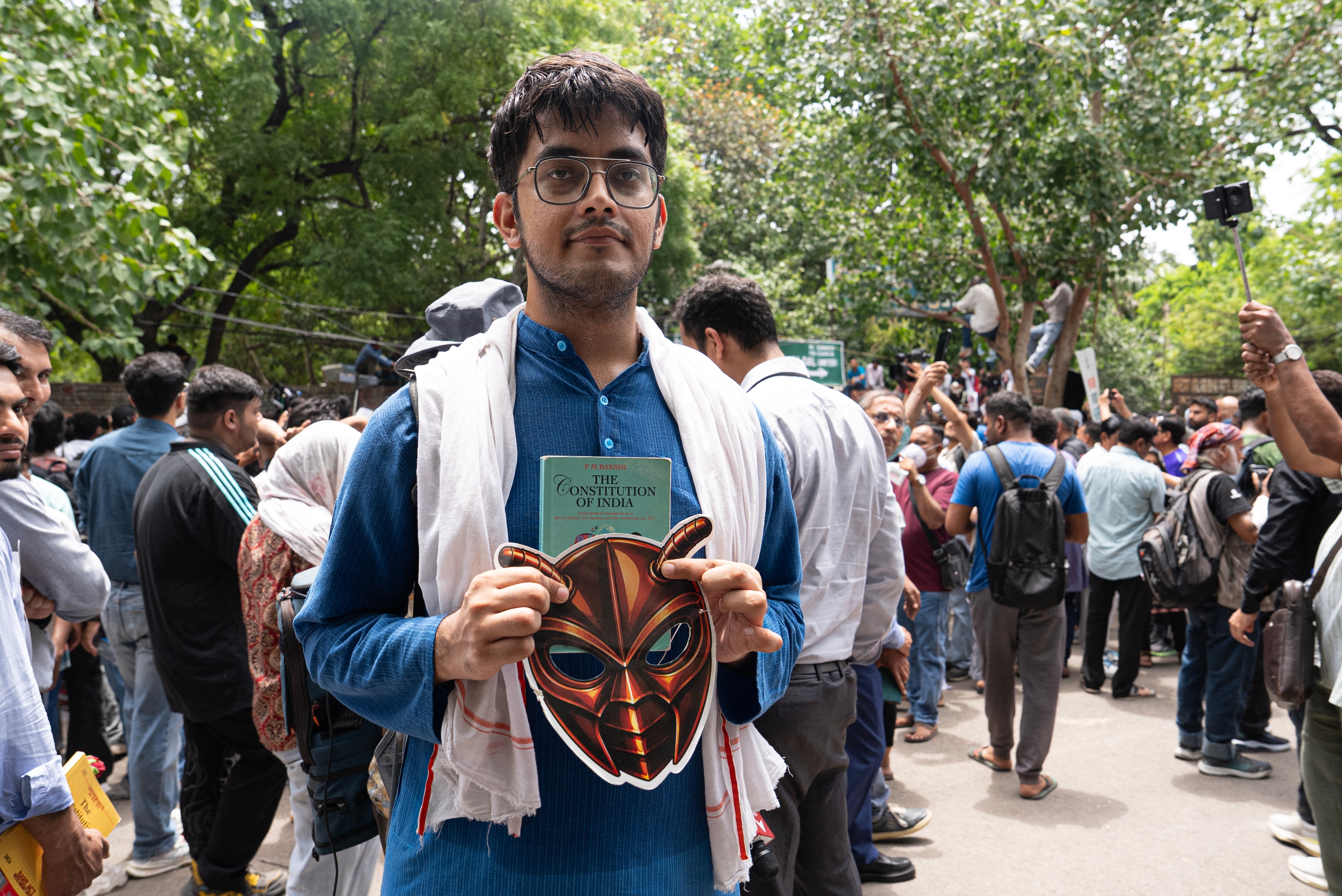 A student protesting holds a cockroach mask and the Indian constitution