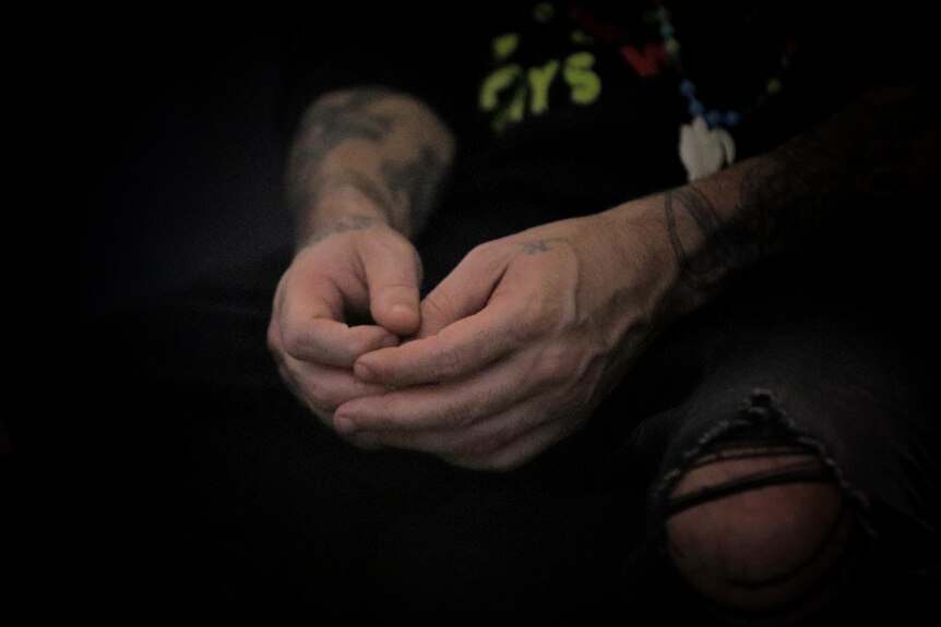 Male's hands resting on his thighs. He has tattoos on his forearm.