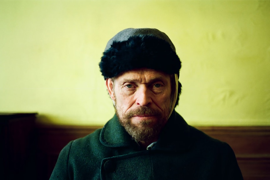 Colour still of Willem Dafoe sitting in front of yellow wall as Vincent Van Gogh in 2018 film At Eternity's Gate.