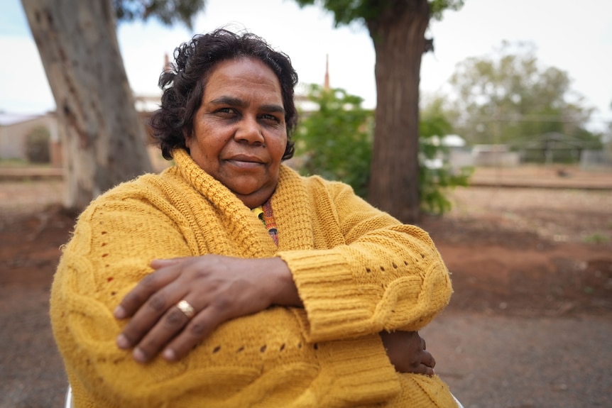 A woman sits with her arms crossed in a rural area.