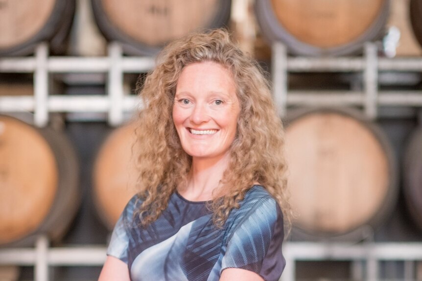 A woman smiling in front of barrels of wine.