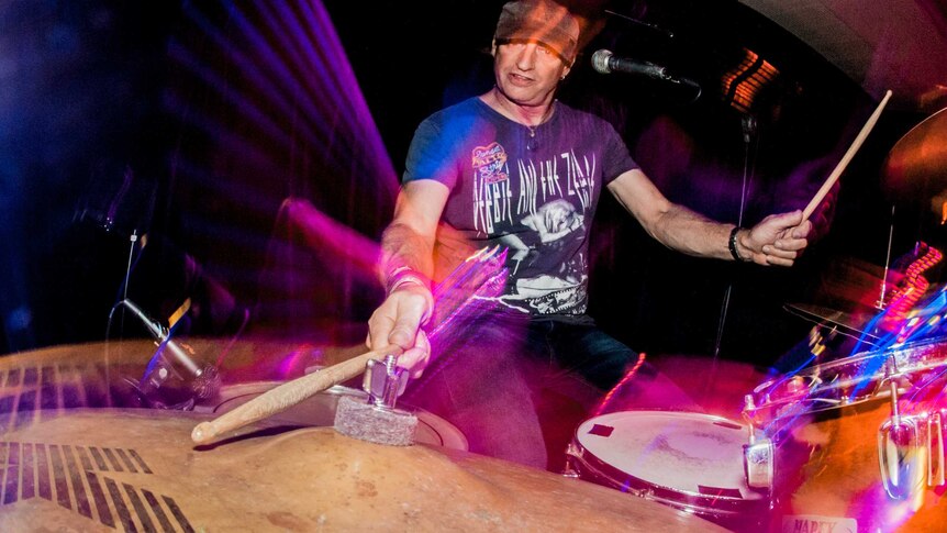 View across a cymbal of a rock drummer playing in a band, one of his drum sticks on the cymbal.
