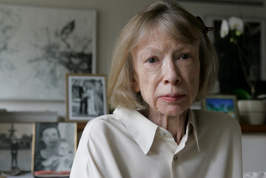 An elderly woman looks at the camera wearing a white shirt. 