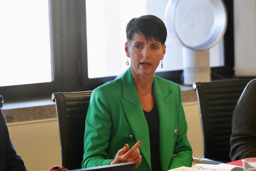 a woman wearing a green blazer sitting at a round table talking