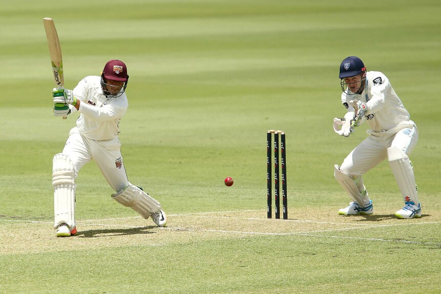 Queensland's Usman Khawaja plays a shot as NSW wicketkeeper Peter Nevill looks on.