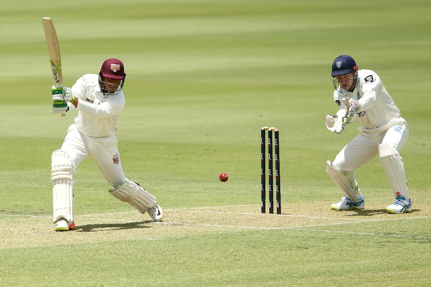 Queensland's Usman Khawaja plays a shot as NSW wicketkeeper Peter Nevill looks on.
