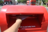 A person posts a letter at a post box in Darwin.