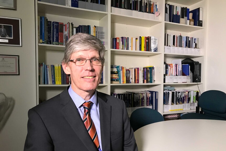 Professor Christopher Fairley sitting in his office in front of a bookshelves.