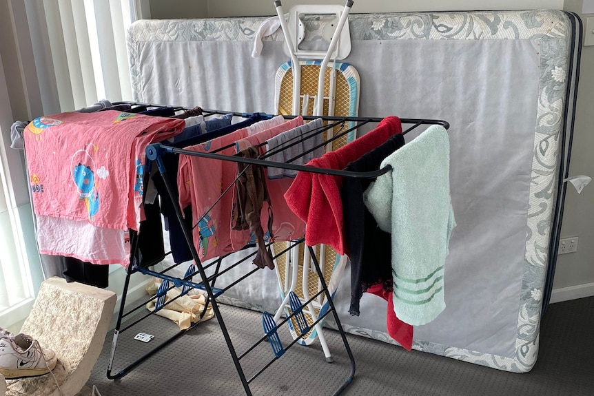 Clothes on a drying rack and mattress against a wall in a livingroom. 