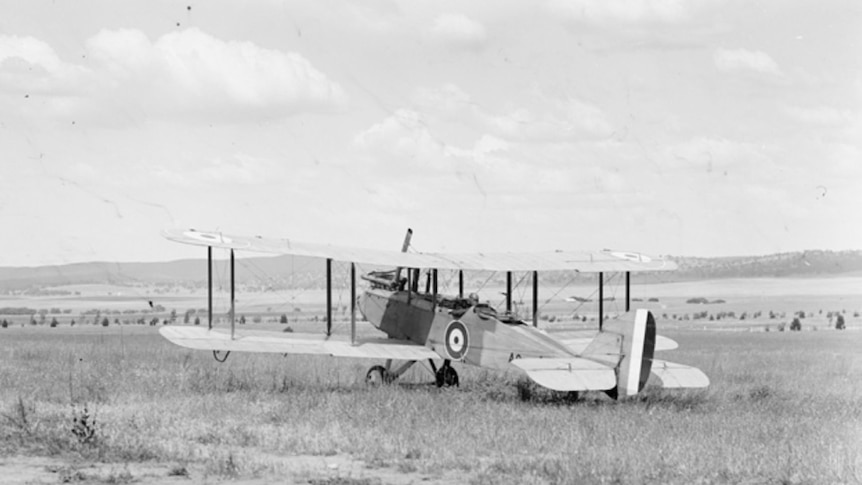 Black and white photo of an old-fashioned plane in the middle of a field.