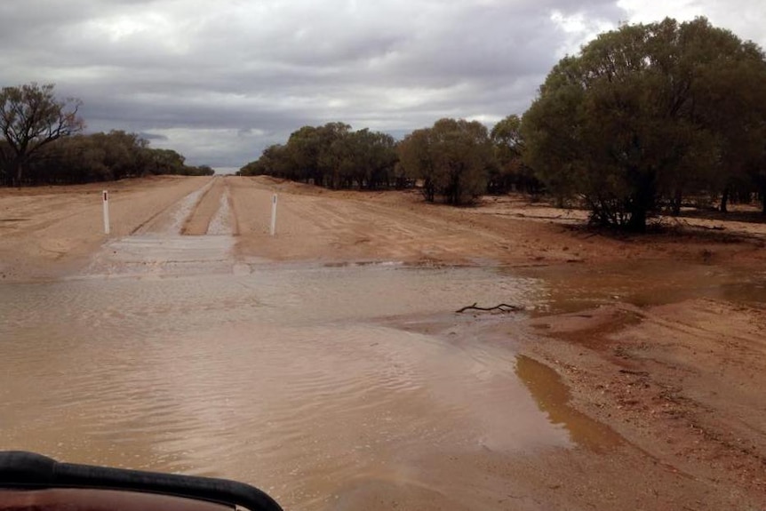 Water spills across an unsealed road.