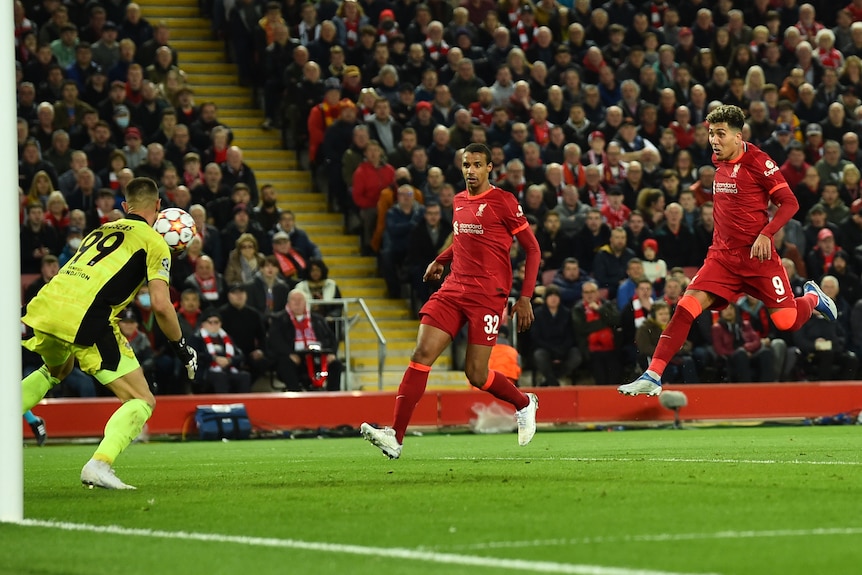 Liverpool's Bobby Firmino (right) jumps through the air as the ball flies past Benfica's goalkeeper.