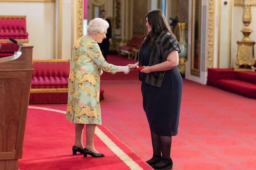 Caitlin shakes hands with Queen Elizabeth in a palace room. 
