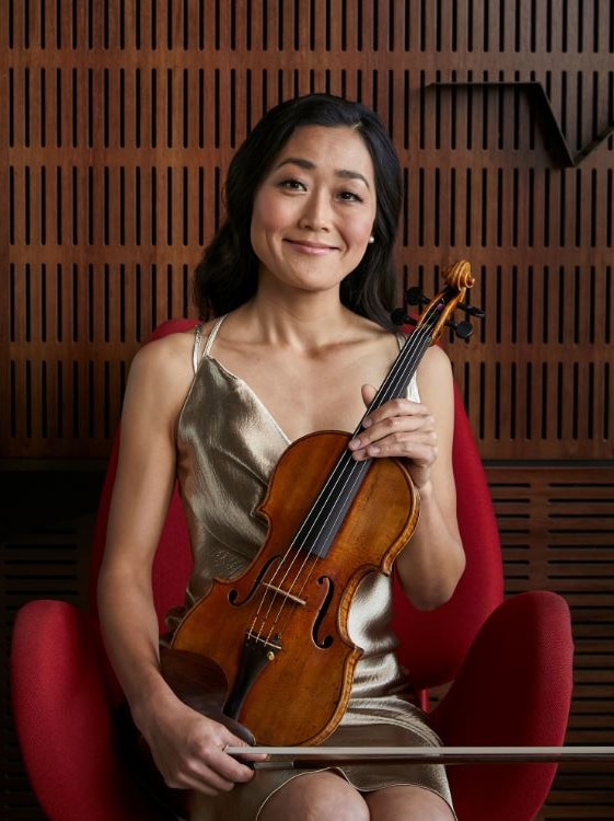 A woman sits in a red chair holding a violin.