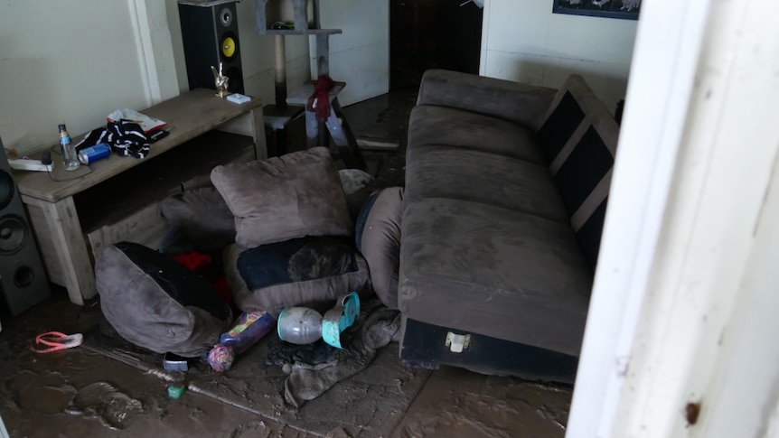 wet mud covers the floor of a lounge room with a family's possessions and couch also in the mud